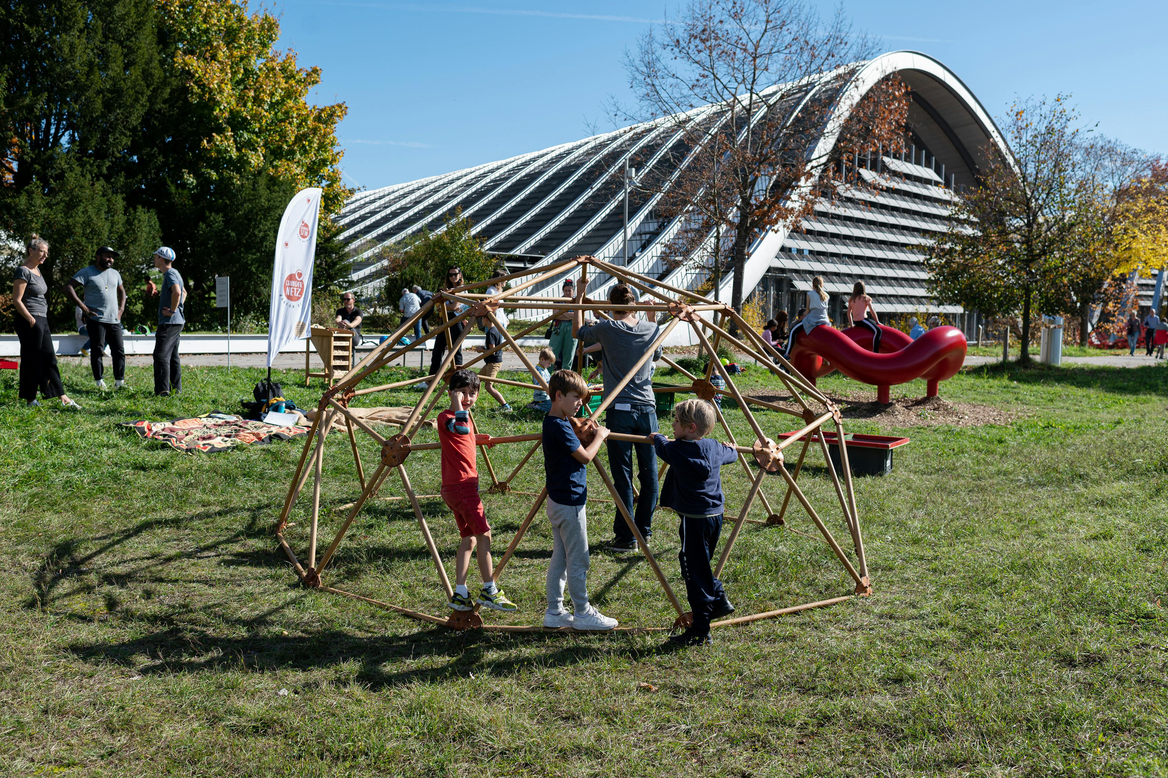 Im Vordergrund sieht man die Spielskulptur Living Dome aus Holz, im Hintergrund das Zentrum Paul Klee.