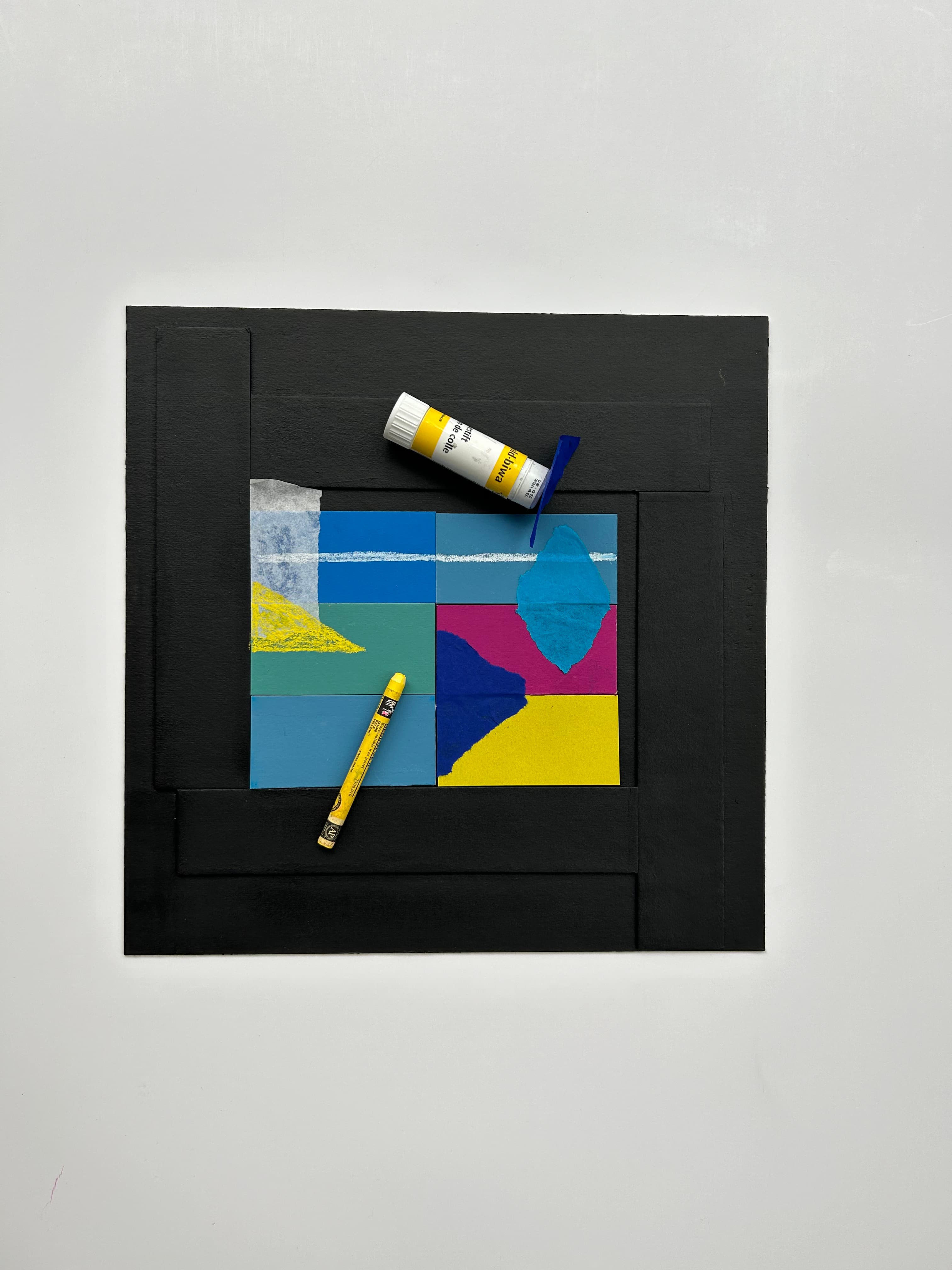 Auf einem schwarzen Papier sind farbig bemalte Rechtecke in gelb, blau und lila. Ein Bunt- und Klebestift liegen daneben.