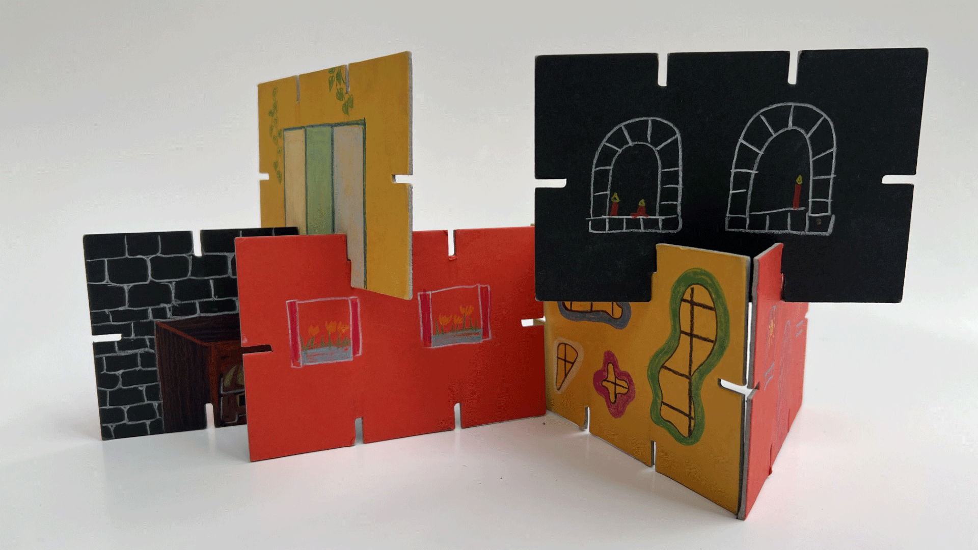 Flache Bauteile aus Karton sind farbig gestaltet und bilden zusammengesteckt ein kleines Haus.