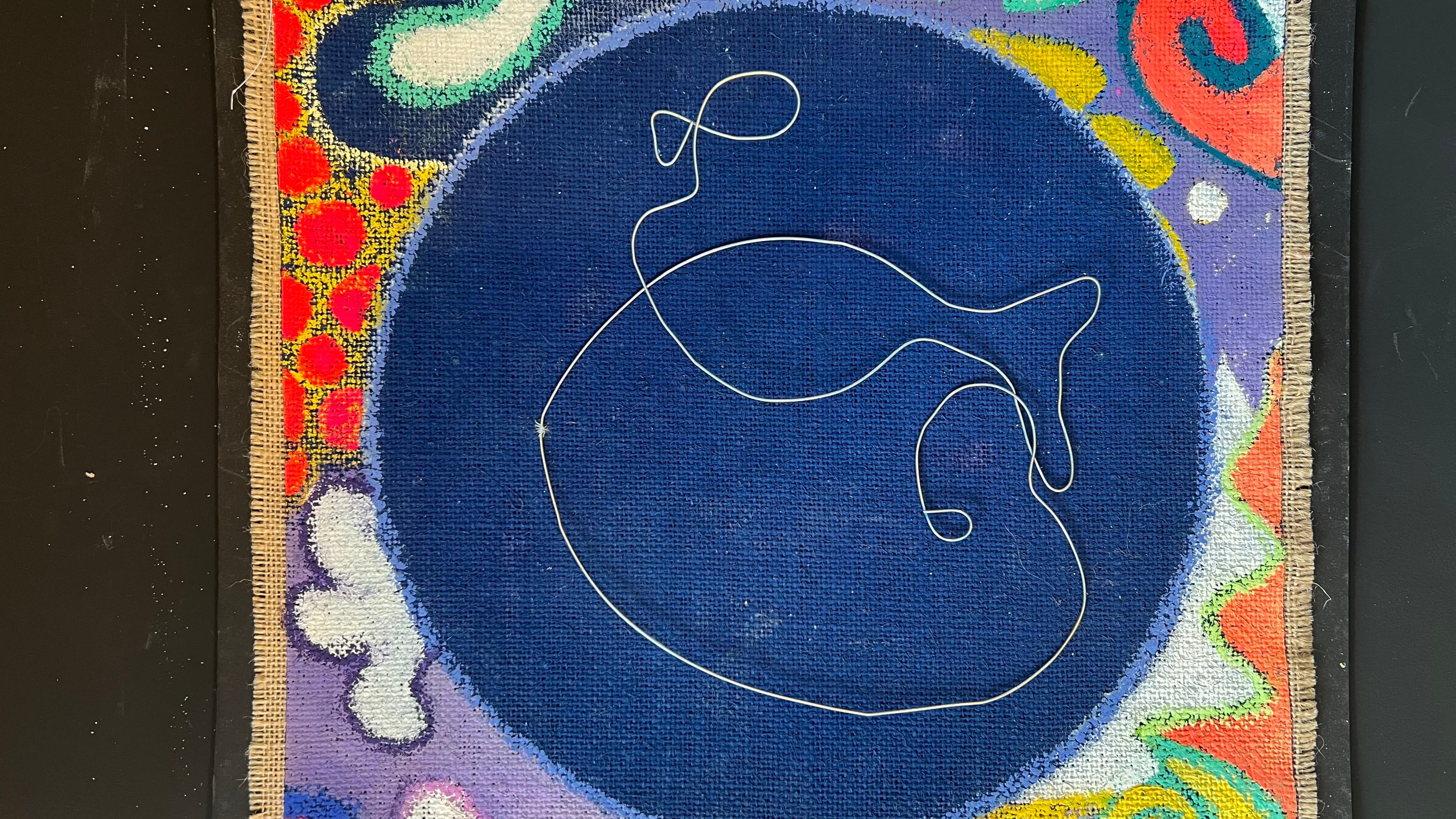 Ein gestaltetes Werk auf Jute mit einem schwungvoll geformten Draht in einem dunkelblauen Kreis