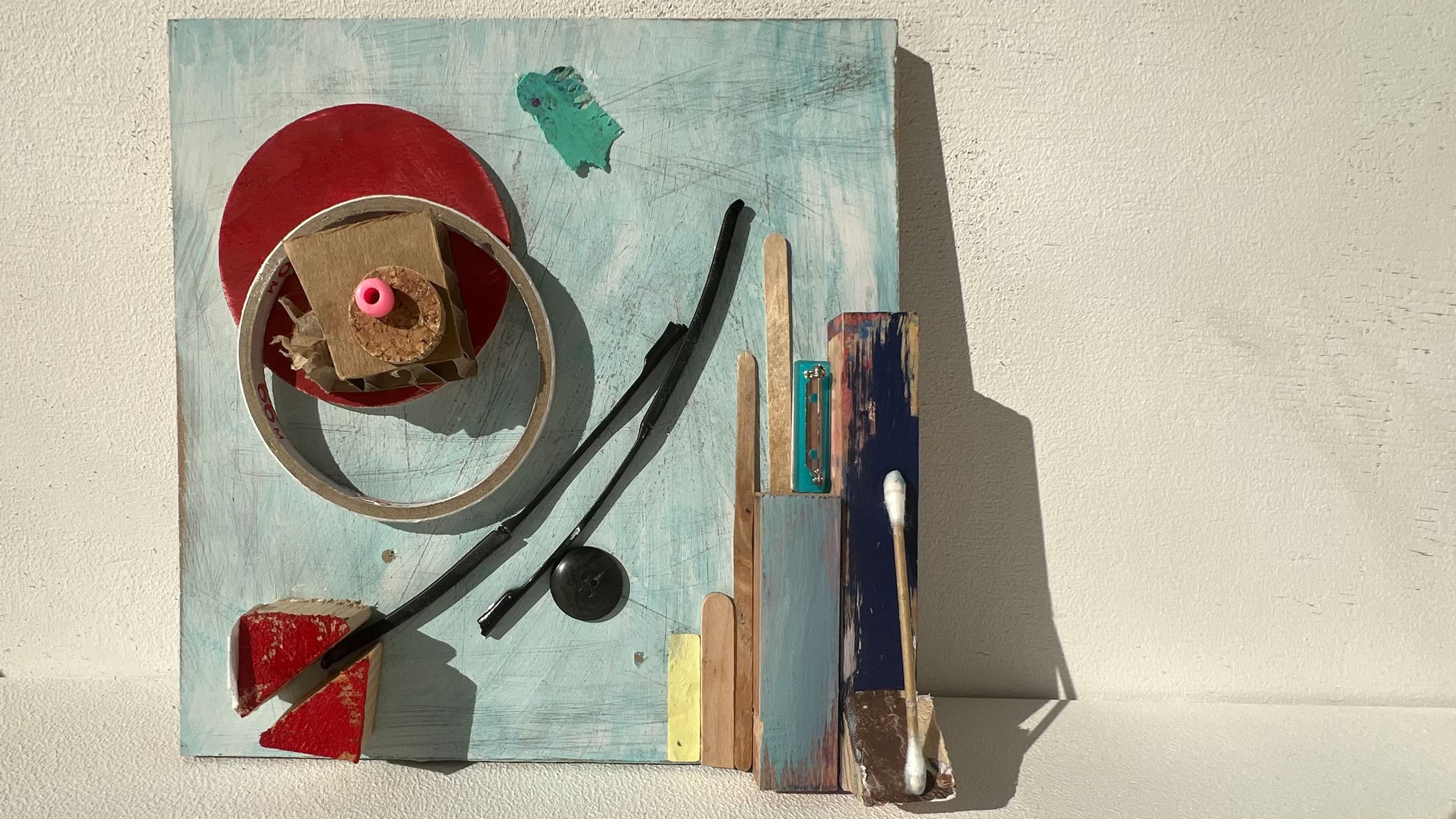 Auf einem Holzstück in 20x20cm sind per Bricollage verschiedene Holzelemente arrangiert.