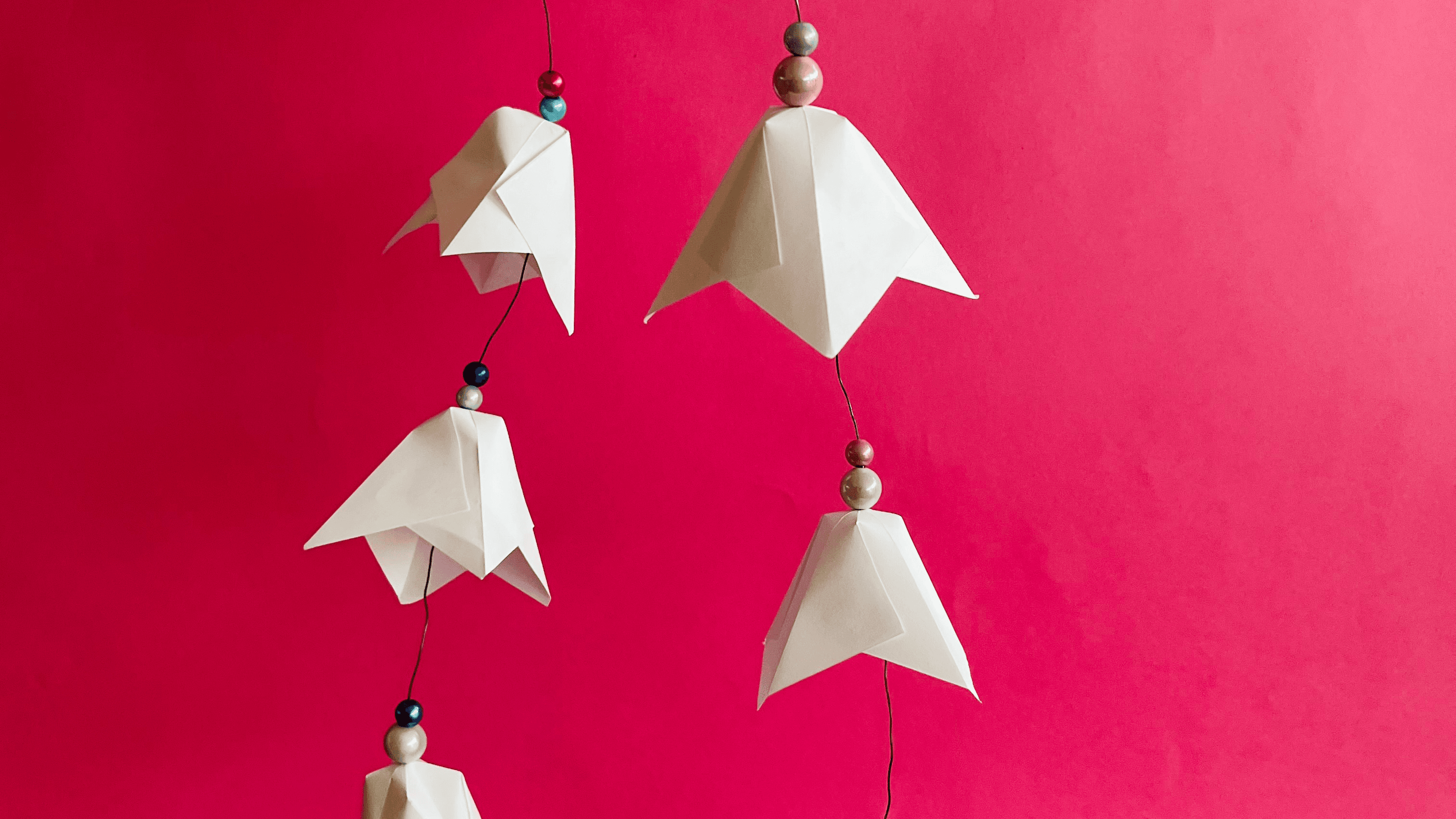 Vor einem leuchtend Hintergrund in Pink sind aus Papier gefaltete Schneeglöckchen an einem Draht aneinandergereiht.
